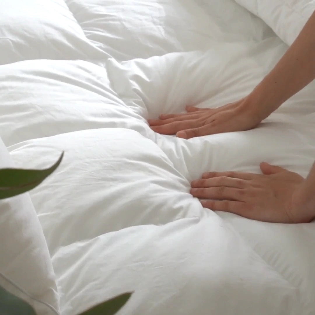 Close-up of a person's hands resting on a fluffy white comforter with a blurred green leaf in the corner.
